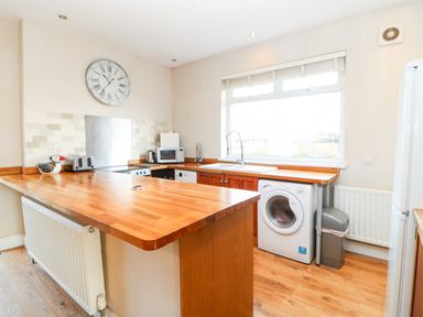 A kitchen with wooden countertops a washing machine a microwave and a large window at Lightkeeper House in Amble-by-the-Sea