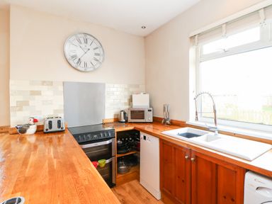 A kitchen with wooden countertops and cabinets a stove microwave toaster and a clock on the wall at Lightkeeper House in Amble-by-the-Sea