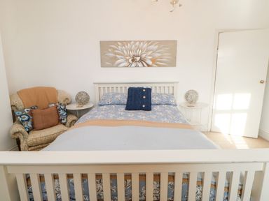 A bedroom with a double bed blue floral bedding armchair with cushions and two round bedside tables at Lightkeeper House in Amble-by-the-Sea