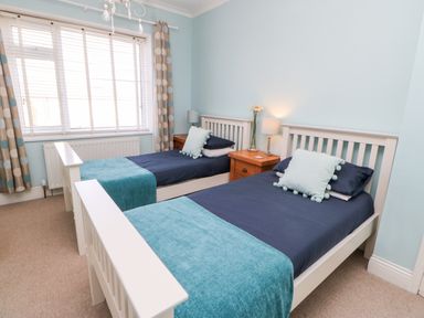 A bedroom with two single beds blue bedding wooden bedside tables and large window at Lightkeeper House in Amble-by-the-Sea