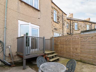 A small outdoor patio area with metal table and chairs next to a raised wooden deck and stairs at Lightkeeper House in Amble-by-the-Sea