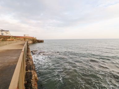 A concrete walkway with railing beside a rocky coastline and ocean at Lightkeeper House in Amble-by-the-Sea