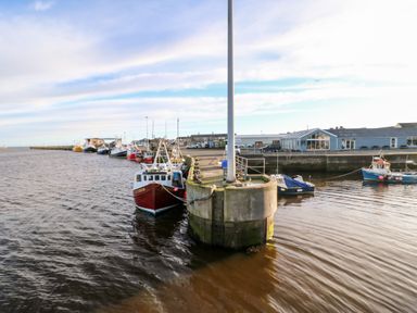 A harbor with several fishing boats docked by a concrete pier at Lightkeeper House in Amble-by-the-Sea