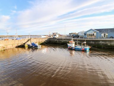 A small harbor with two fishing boats tied to a concrete dock and buildings in the background at Lightkeeper House in Amble-by-the-Sea
