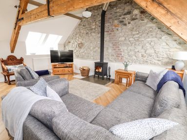 A living room with a grey sofa set a wood burning stove and a television on a wooden stand at Yr Hen Festri in Y Felinheli