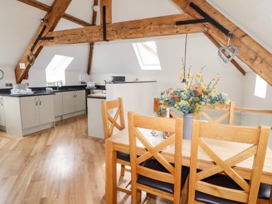 An open kitchen with cupboards and a dining table with chairs and a flower arrangement at Yr Hen Festri in Y Felinheli