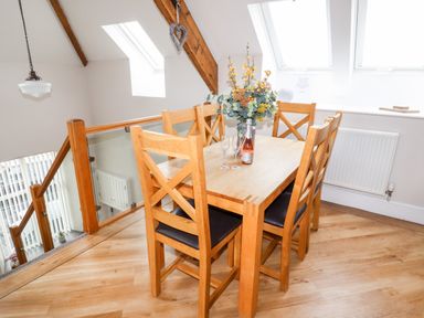 A dining area with a wooden table and six chairs a flower arrangement and a bottle with two glasses at Yr Hen Festri in Y Felinheli