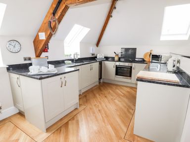 A kitchen with wooden beams a clock and black countertops at Yr Hen Festri in Y Felinheli