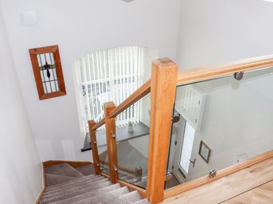 A staircase with wooden handrails and glass panels leading down to a door with a window beside a stained glass picture on the wall at Yr Hen Festri in Y Felinheli