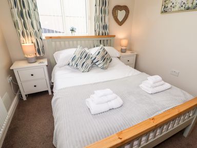 A bedroom with a double bed two bedside tables with lamps and folded towels on the bed at Yr Hen Festri in Y Felinheli