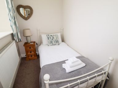 A small bedroom with a single bed a bedside table with a lamp and a heart-shaped mirror at Yr Hen Festri in Y Felinheli