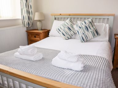 A bed with white linens and patterned pillows with folded towels on it beside wooden nightstands with a lamp at Yr Hen Festri in Y Felinheli