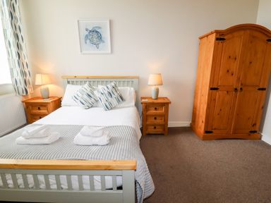 A bedroom with a double bed with pillows and towels bedside tables with lamps a wooden wardrobe and a turtle picture on the wall at Yr Hen Festri in Y Felinheli