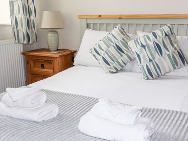 A bedroom with a bed with white sheets and patterned pillows with folded towels on top at Yr Hen Festri in Y Felinheli