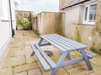 A patio area with a grey wooden picnic table and benches beside a building at Yr Hen Festri in Y Felinheli