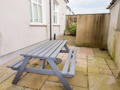 An outdoor patio area with a gray picnic table and bench on stone paving at Yr Hen Festri in Y Felinheli