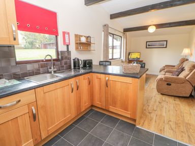 A kitchen with wooden cabinets and a black countertop open to a living room with three brown recliner chairs and a television at Bluebell Lodge in Saltburn-by-the-Sea