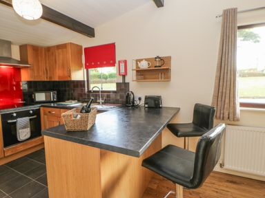 A kitchen with a countertop, two black bar stools, cabinets, oven, microwave, and window at Bluebell Lodge in Saltburn-by-the-Sea