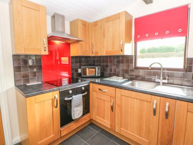A kitchen with wooden cabinets black countertop black tiled backsplash and a red window blind at Bluebell Lodge Saltburn-by-the-Sea