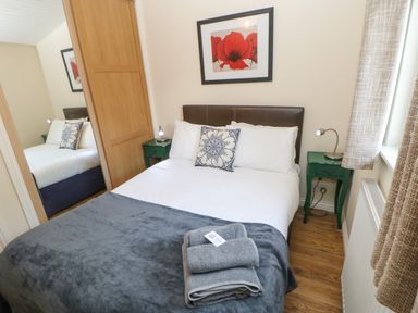 A bedroom with a double bed white and grey bedding bedside tables lamps a framed flower picture and wooden floor at Bluebell Lodge in Saltburn-by-the-Sea