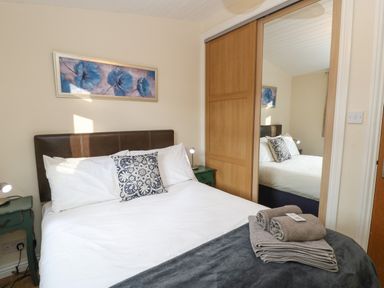 A bedroom with a bed a blue and white cushion a green bedside table and a wooden wardrobe with mirror at Bluebell Lodge in Saltburn-by-the-Sea