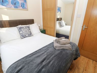 A bedroom with a bed a pillow a gray blanket folded towels a wooden door and a wardrobe with a mirror at Bluebell Lodge in Saltburn-by-the-Sea