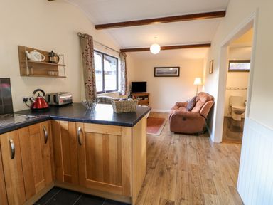 A kitchen area with wooden cabinets, a red kettle, a toaster, and a living room with a brown reclining chair, a TV, and a floor lamp at Violet Lodge in Saltburn-by-the-Sea