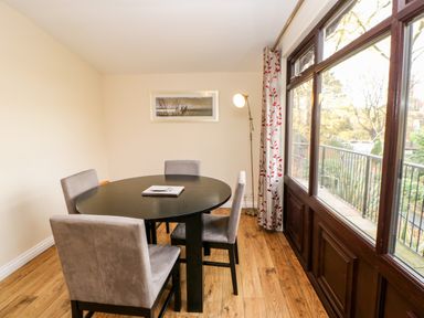 A dining room with a round black table and four chairs next to large windows at Violet Lodge in Saltburn-by-the-Sea