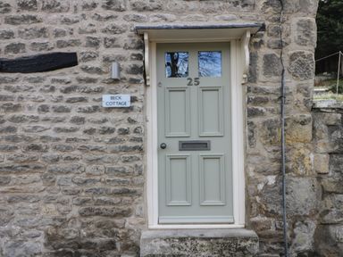 A light green front door with number 25 and mail slot on a stone wall with a sign saying Beck Cottage in Pickering