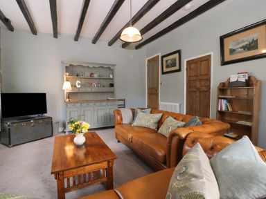 A living room with brown leather sofas a wooden coffee table a tv on a chest and a grey cabinet at Beck Cottage in Pickering