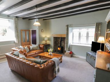 A living room with leather sofas a wooden coffee table a wood burning stove and a television at Beck Cottage in Pickering