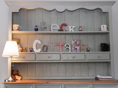 A wooden cabinet with shelves holding decorative letters spelling Beck Cottage a lamp on the left and books on the right