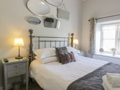 A bedroom with a metal bed frame white bedding grey pillows two bedside tables with lamps and a window with curtains at Beck Cottage in Pickering