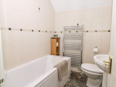A bathroom with a bathtub toilet sink wooden shelf and heated towel rail at Beck Cottage in Pickering