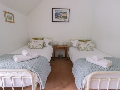 A bedroom with two single beds separated by a wooden bedside table and framed pictures on white walls at Beck Cottage in Pickering