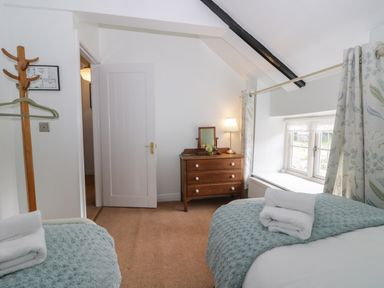 A bedroom with two beds a wooden dresser a lamp a window with curtains and a coat rack at Beck Cottage in Pickering