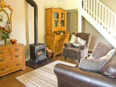 A living room with wood stove wooden furniture armchair leather sofa and staircase at Carreg Rhys Malltraeth near Newborough