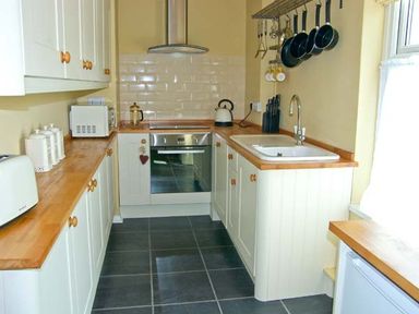 A kitchen with white cabinets wooden countertops a sink stove microwave and hanging pans at Carreg Rhys in Malltraeth near Newborough
