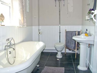 A bathroom with a clawfoot bathtub a toilet a pedestal sink a towel rack and a window at Carreg Rhys in Malltraeth near Newborough