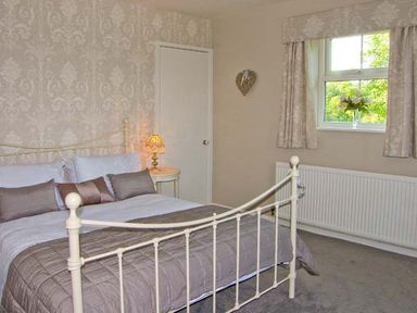 A bedroom with a bed a nightstand with a lamp a window with curtains and a radiator at Carreg Rhys in Malltraeth near Newborough