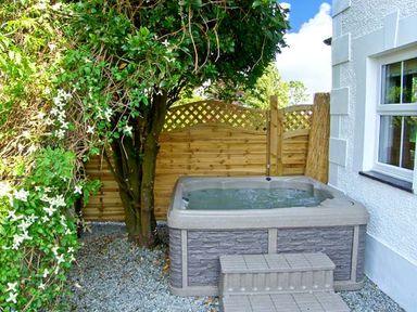 An outdoor hot tub next to a house with a small tree and wooden fence at Carreg Rhys in Malltraeth near Newborough