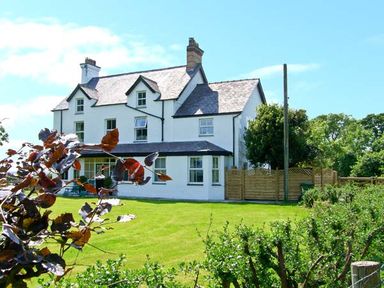 A white multi-story house with a slate roof and garden at Carreg Rhys in Malltraeth near Newborough