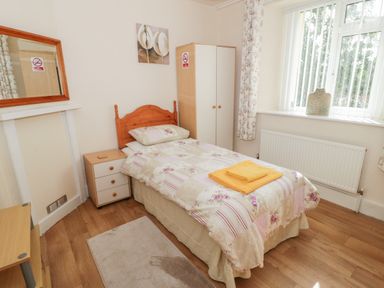 A bedroom with a single bed with floral bedding yellow towels on the bed a bedside table wardrobe mirror and a window at Bangor Cottage in Bangor