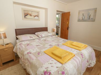 A bedroom with a double bed with floral quilt two yellow towels bedside tables with lamps and two paintings on the walls at Bangor Cottage in Bangor