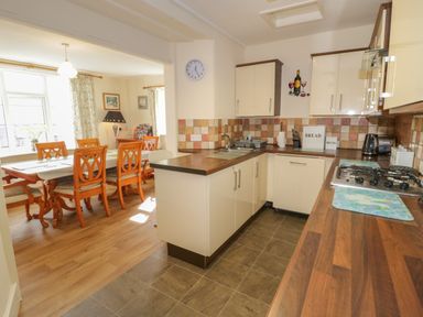 A kitchen with cabinets countertops a sink stove and an adjoining dining area with a wooden table and chairs at Bangor Cottage in Bangor
