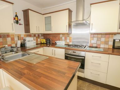 A kitchen with wooden countertops white cabinets a stainless steel sink a gas stove and oven a yellow toaster and labeled containers at Bangor Cottage Bangor