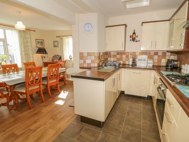 A kitchen with cream cabinets and a dining area with wooden chairs at Bangor Cottage in Bangor