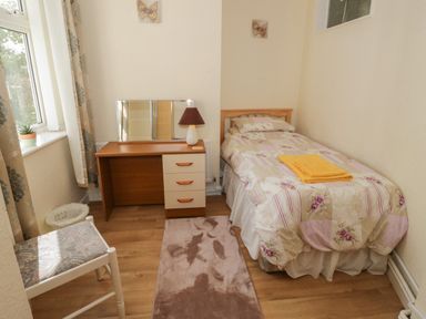 A small bedroom with a single bed with floral bedding and yellow towels a wooden desk with a mirror and lamp a chair a small plant on the window at Bangor Cottage in Bangor