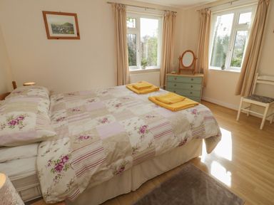 A bedroom with a bed covered in floral bedspread and two yellow towels on top a chest of drawers with a mirror a chair and two windows at Bangor Cottage in Bangor