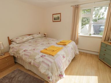 A bedroom with a double bed with patterned bedding two yellow towels on the bed bedside tables and lamps a window with curtains and a chest of drawers at Bangor Cottage in Bangor